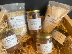 KI generiert: Das Bild zeigt eine Auswahl von Kastanienprodukten der Marke "La Ferme des Ducs", darunter Marmeladen, Mehl und ganze Kastanien, arrangiert auf einer Unterlage aus Stroh. Hauptinhalt des Bildes sind die biozertifizierten Produkte, die in Gläsern und Beuteln verpackt sind.