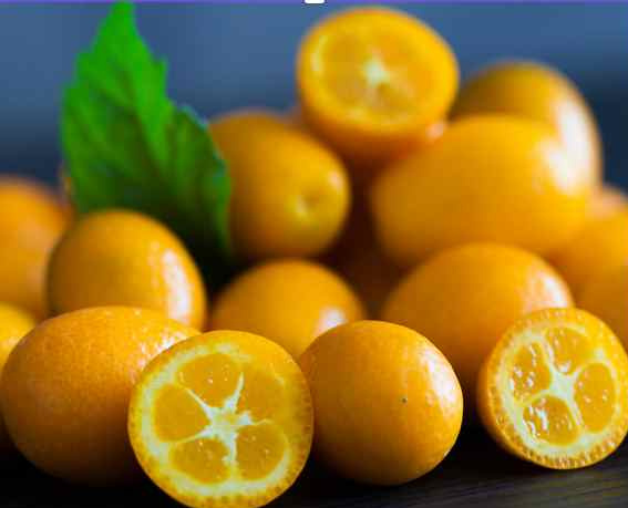 KI generiert: Das Bild zeigt eine Ansammlung von Kumquats, wobei einige Früchte angeschnitten sind, um das innere Fruchtfleisch sichtbar zu machen. Im Hintergrund ist ein grünes Blatt zu sehen.