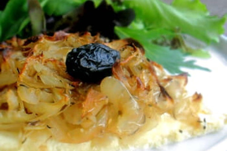 KI generiert: Das Bild zeigt ein gebackenes Gericht aus Kartoffeln und möglicherweise weiteren Zutaten wie Zwiebeln und Gemüse in einer rechteckigen Form. Eine Gabel und ein Löffel liegen darauf.