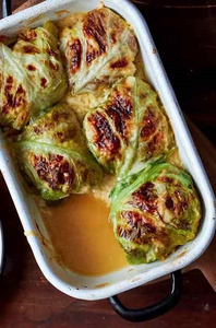 KI generiert: Das Bild zeigt eine Auflaufform mit gebratenen Kohlrouladen, die in einer bräunlichen Soße liegen. Der Hauptinhalt des Bildes sind die goldbraun gebackenen Rouladen.