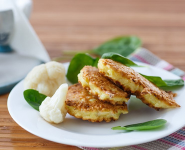 KI generiert: Das Bild zeigt drei goldbraune Puffer auf einem weißen Teller, garniert mit Spinatblättern und Blumenkohlstücken. Der Fokus liegt auf den appetitlich angerichteten Puffern.