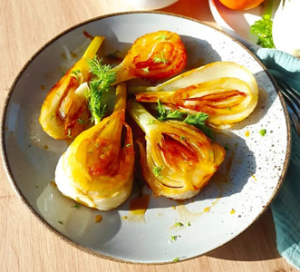KI generiert: Das Bild zeigt ein Gericht mit karamellisiertem Fenchel in einer Schale. Der Fenchel ist appetitlich angerichtet und mit einigen grünen Kräutern garniert.