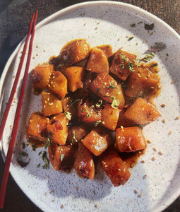 KI generiert: Das Bild zeigt ein gebackenes Gericht aus Kartoffeln und möglicherweise weiteren Zutaten wie Zwiebeln und Gemüse in einer rechteckigen Form. Eine Gabel und ein Löffel liegen darauf.