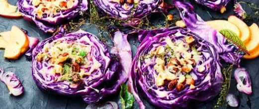 KI generiert: Das Bild zeigt kunstvoll angerichtete Scheiben von Rotkohl, die mit verschiedenen Zutaten gefüllt sind. Ringsherum sind dekorative Garnituren und Kräuter zu sehen.